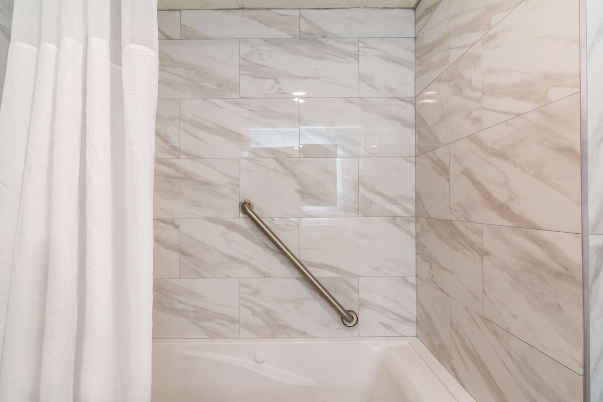 Un baño con suelo de mármol, barandilla y bañera.