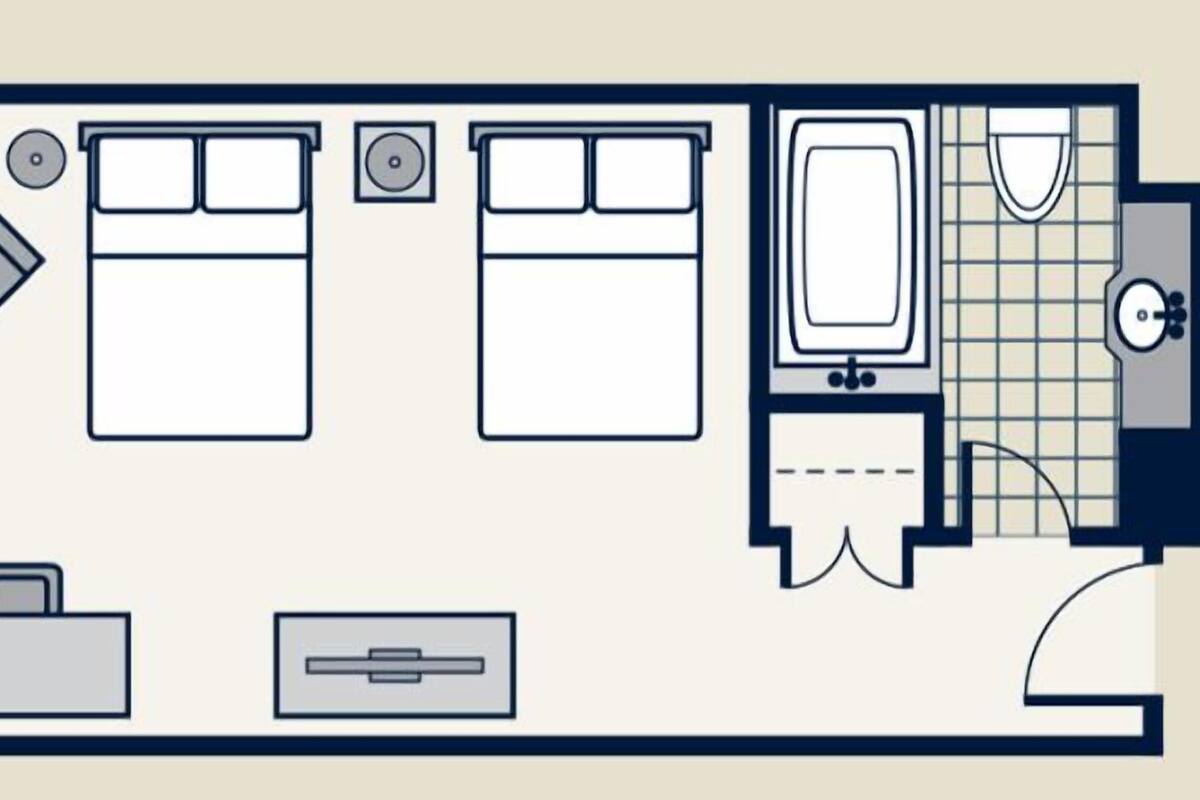 Distribución de una habitación de hotel con cama, escritorio, silla, baño pequeño y maleta.