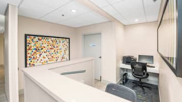 A reception area with a white reception desk, a colorful geometric wall art, a closed door, and a computer desk with a chair.