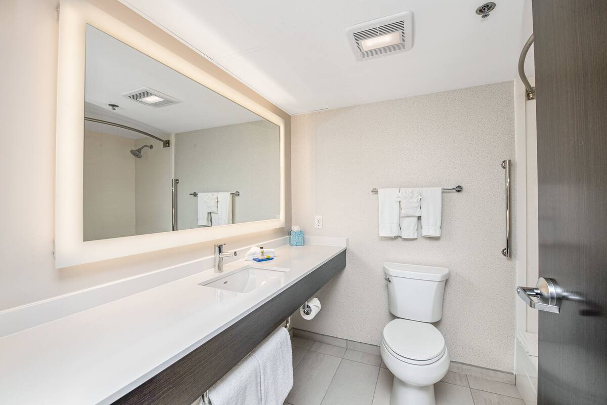 A modern bathroom with a large mirror, a sink, a toilet, and a shower.