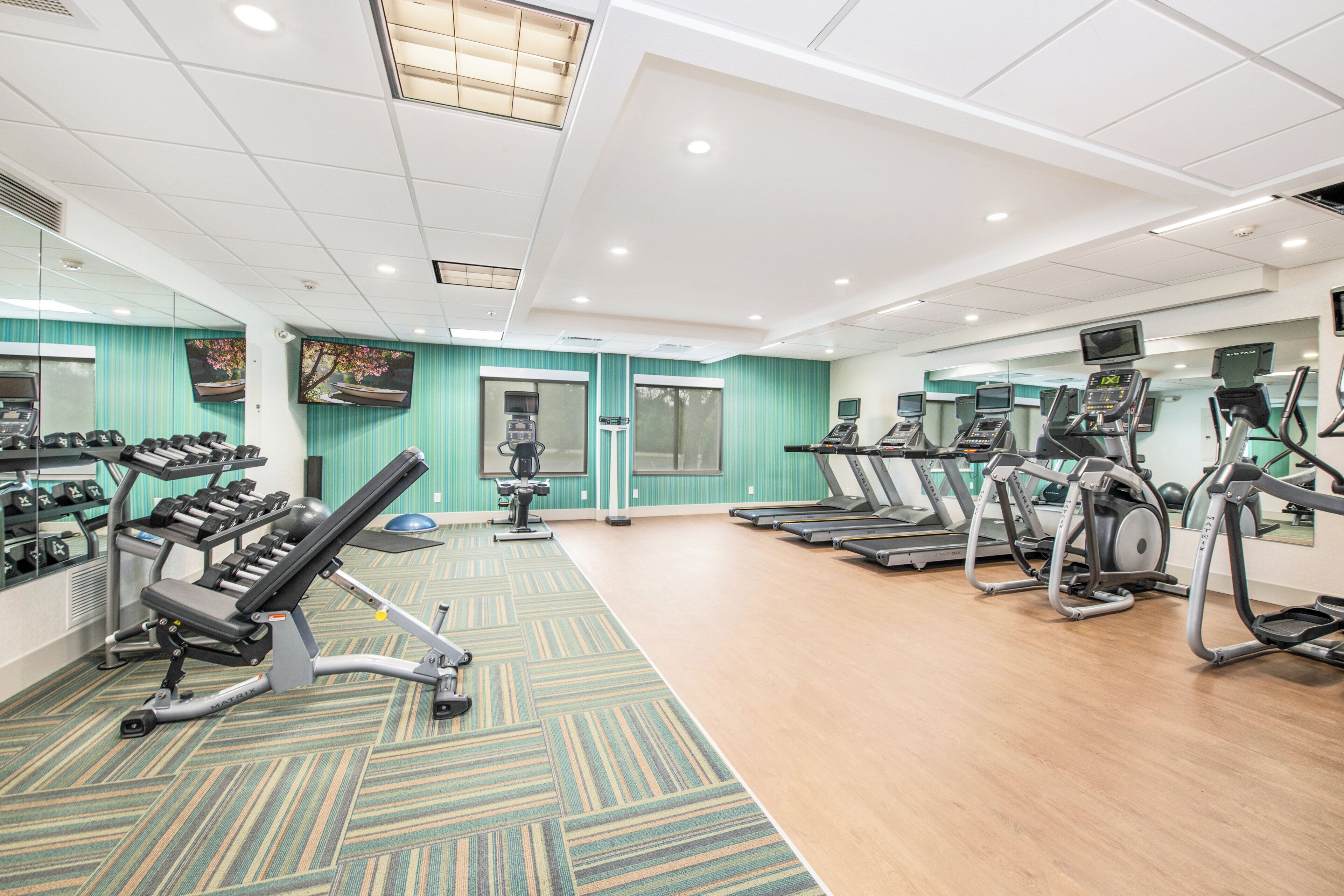 Een fitnessruimte met loopbanden, elliptische trainers en losse gewichten.