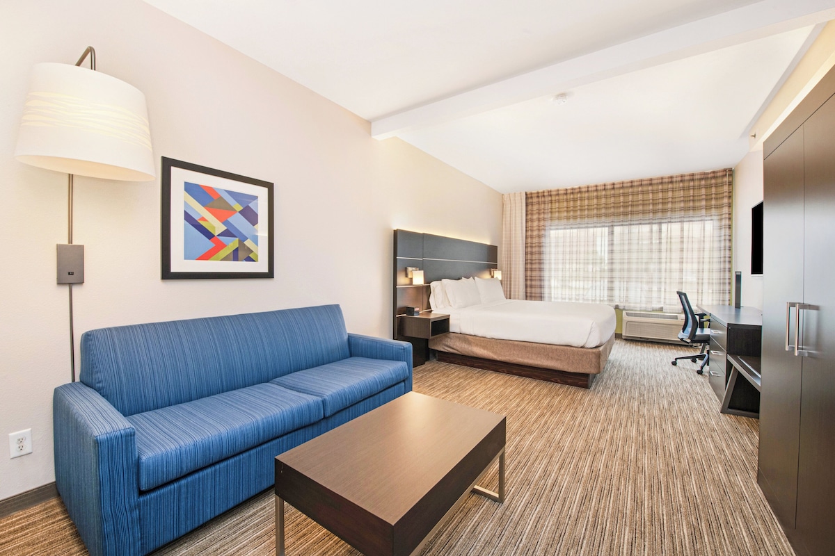 A hotel room with a blue sofa, a bed, a desk, a lamp, and a framed picture on the wall.