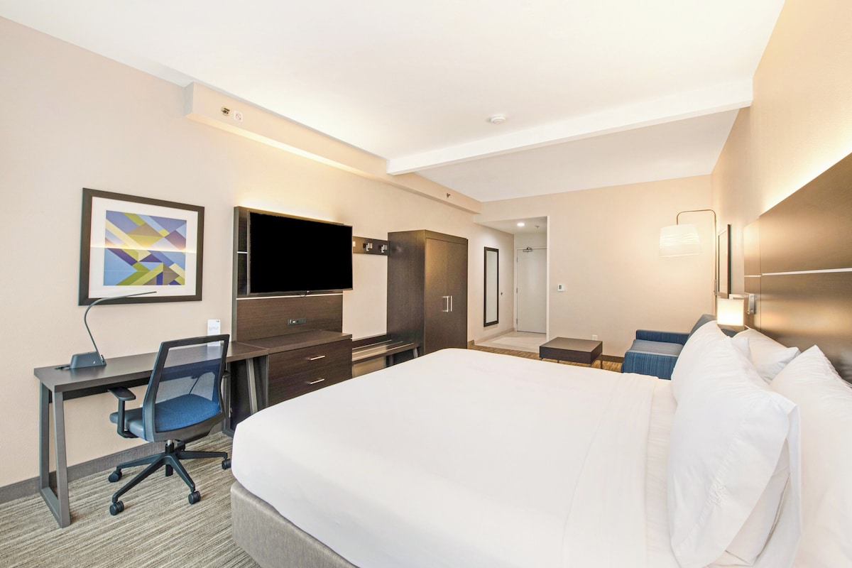 A hotel room with a bed, desk, chair, television, wardrobe, and a bathroom.