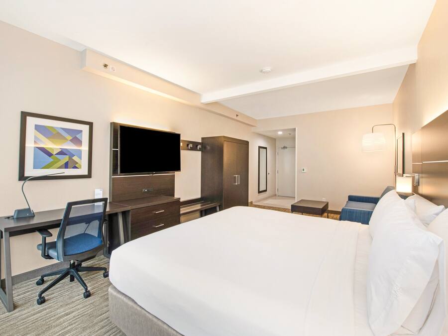 Habitación de hotel con una cama grande, un escritorio con silla, televisor, armario y puerta al baño.