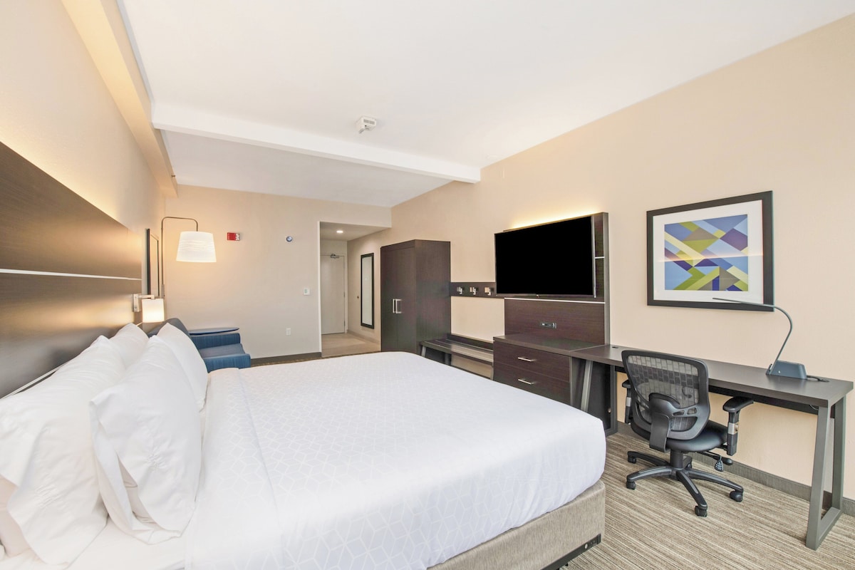 A hotel room with a large bed, a desk with a chair, a flat-screen TV, and a framed abstract painting on the wall.