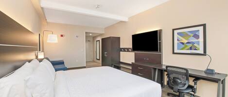 A hotel room with a large bed, a desk with a chair, a flat-screen TV, and a framed abstract painting on the wall.