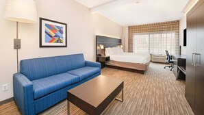 A hotel room with a blue sofa, a bed, a desk, a lamp, and a framed abstract artwork. - Holiday Inn Express & Suites Delafield by IHG (Delafield)