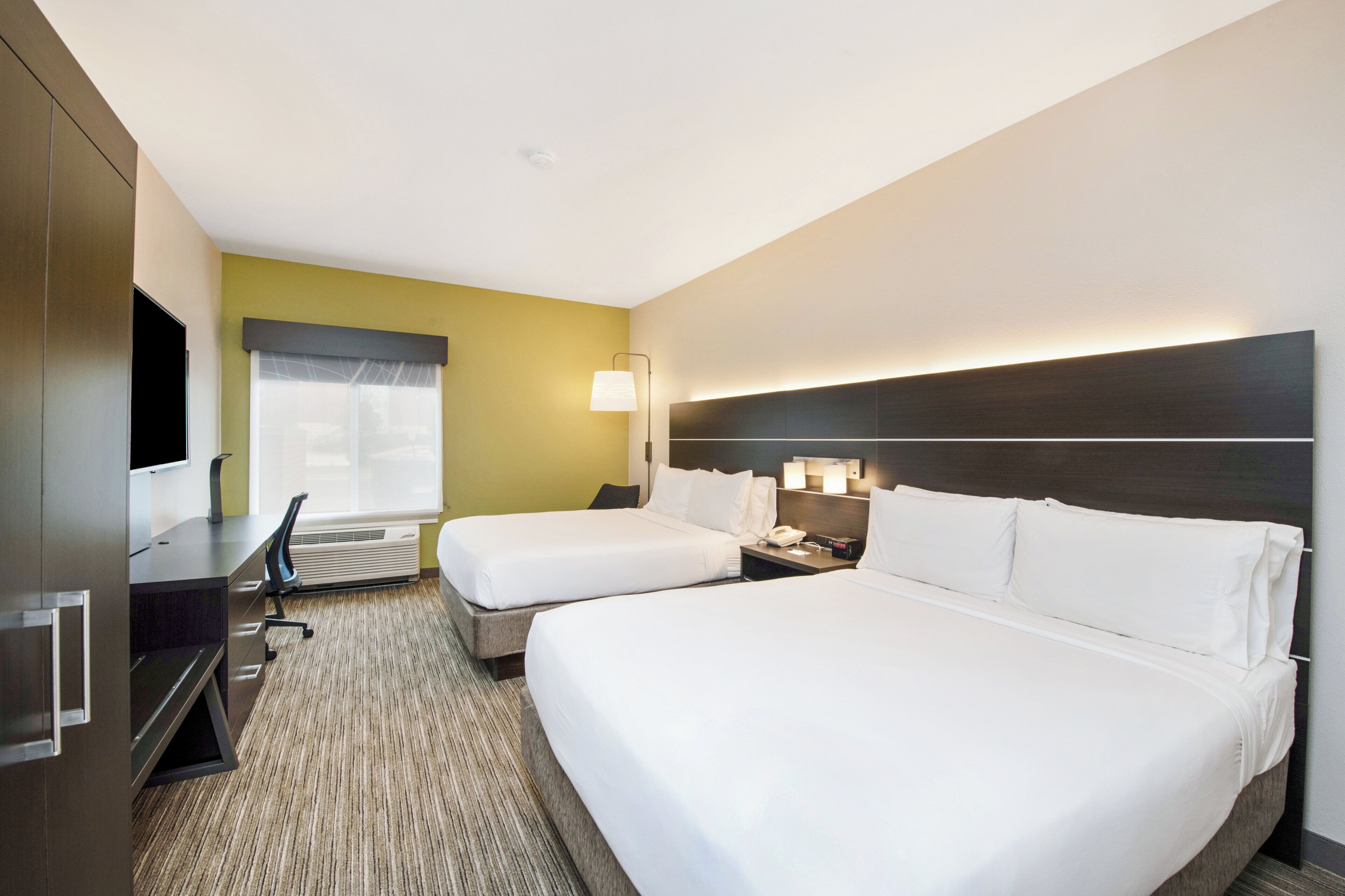 A hotel room with two beds, a desk, a chair, a TV, and a window with blinds.