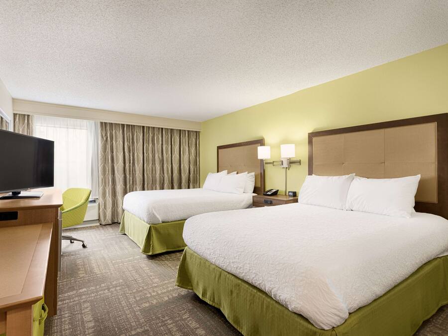 Une chambre d’hôtel avec deux lits, un bureau avec une télévision, une chaise et une fenêtre avec des rideaux.