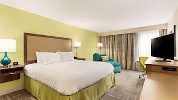 Une chambre d’hôtel avec un grand lit, un bureau avec une télévision, une chaise et une fenêtre avec des rideaux.