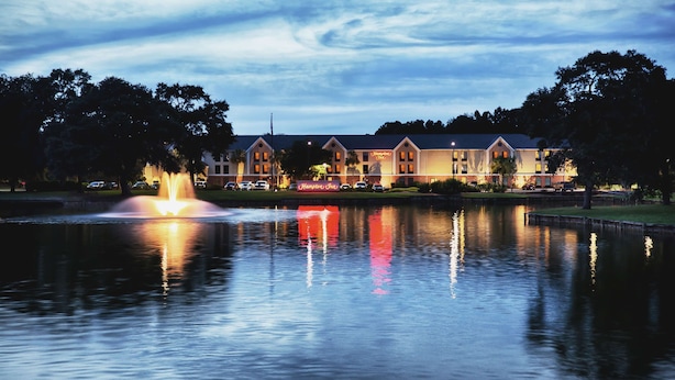 Un hotel con una gran fuente frente a él, rodeado de árboles y una masa de agua tranquila que refleja las luces.