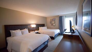 A hotel room with two beds, a desk, a chair, a TV, and a window with curtains.