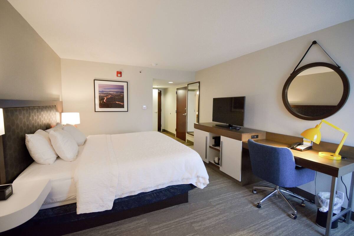 A hotel room with a bed, desk, chair, TV, and a mirror.