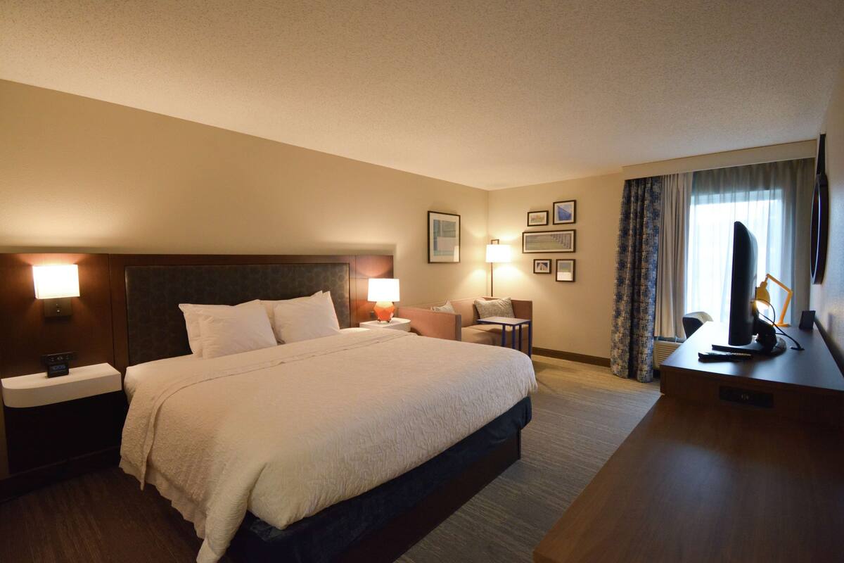 A hotel room with a large bed, bedside tables with lamps, a desk, and a television.