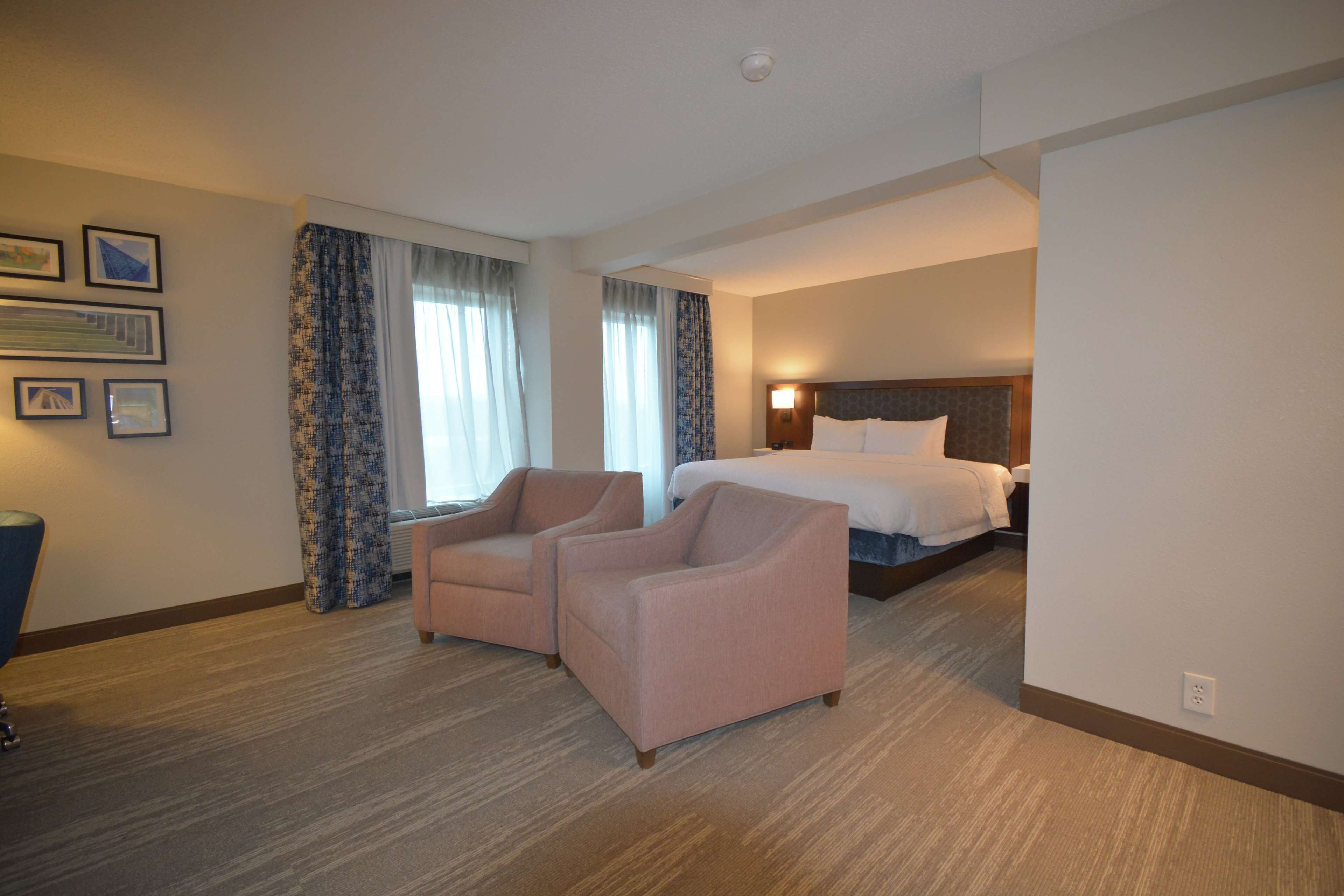 A hotel room with a bed, two armchairs, a desk, and a window with curtains.