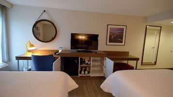 A hotel room with two beds, a desk with a computer, a TV, a desk lamp, a mirror, and a framed picture on the wall.