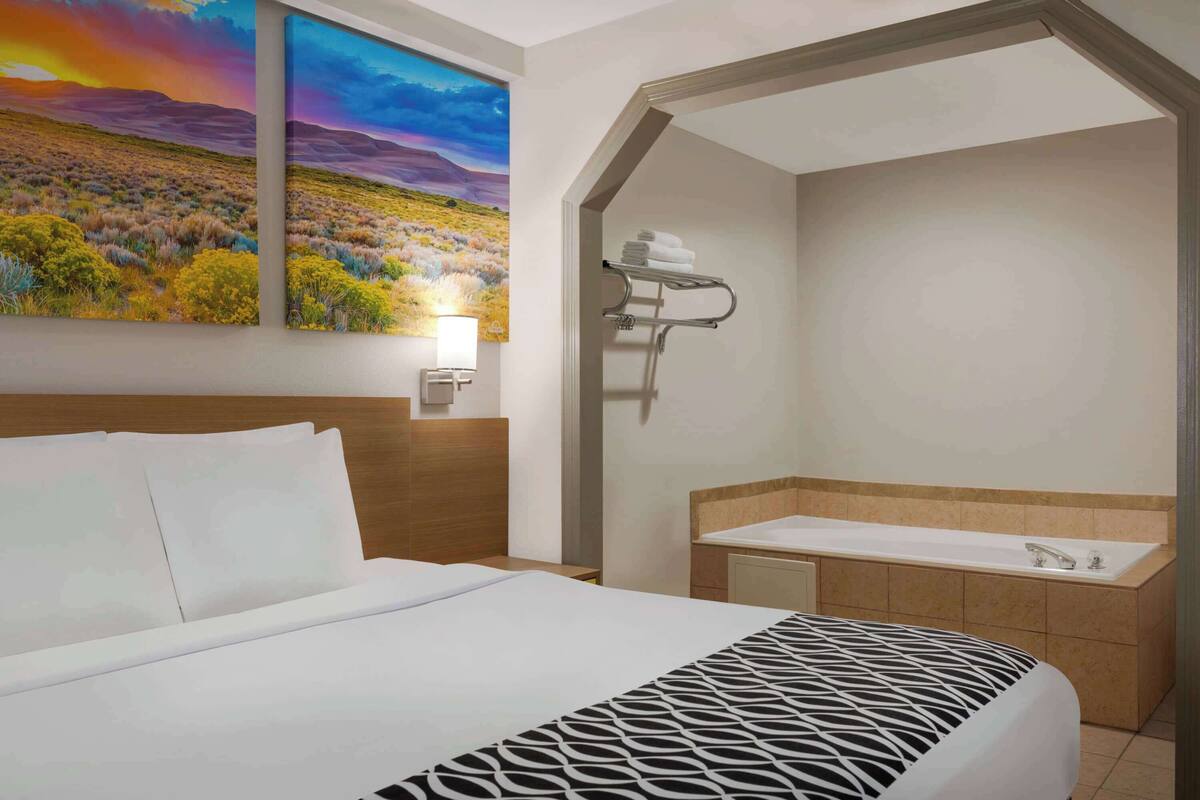 Ein Hotelzimmer mit Bett, einem Badezimmer mit Badewanne und zwei Bildern an der Wand.