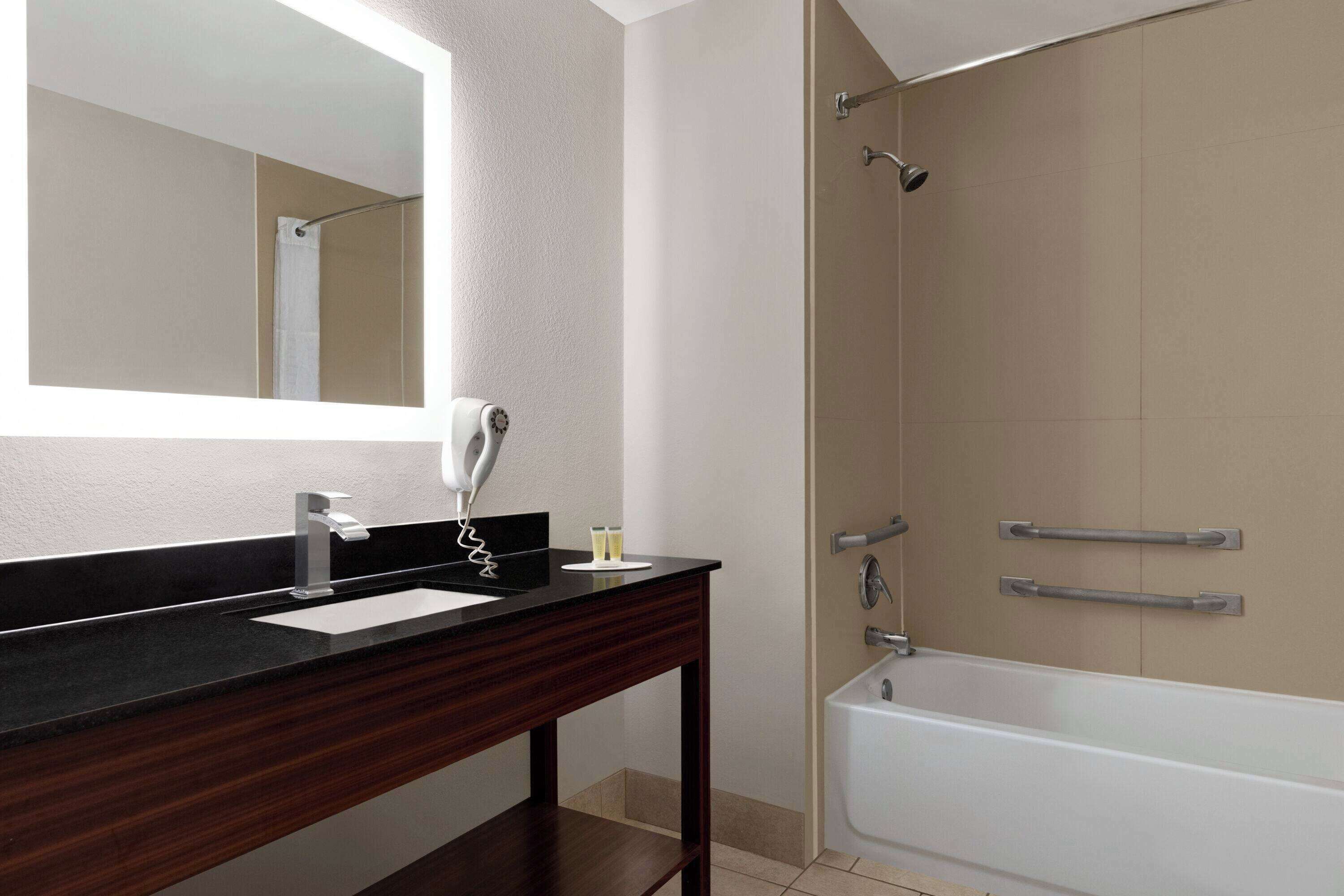 A bathroom with a dark wood vanity, a mirror, a white sink, and a bathtub.