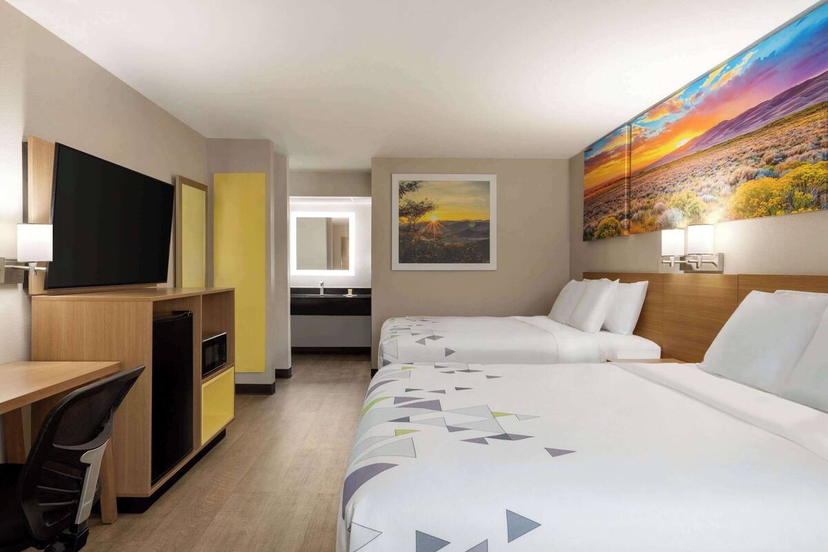 Ein Hotelzimmer mit zwei Betten, einem Schreibtisch, einem Fernseher und einem Bild an der Wand.