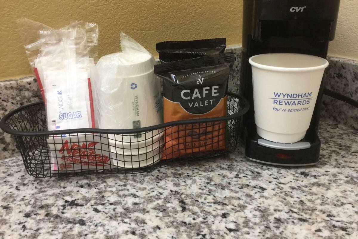 Eine Kaffeemaschine, eine Tasse Kaffee, ein Korb mit Zucker, Servietten und einer Kaffeepackung.
