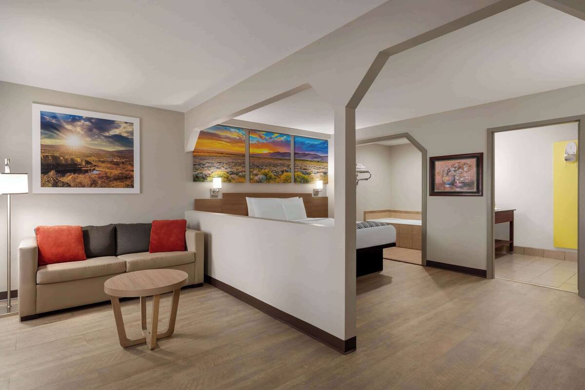 Ein Hotelzimmer mit einer Couch, einem runden Tisch, einem Bett und einem Gemälde einer Sonnenlandschaft.