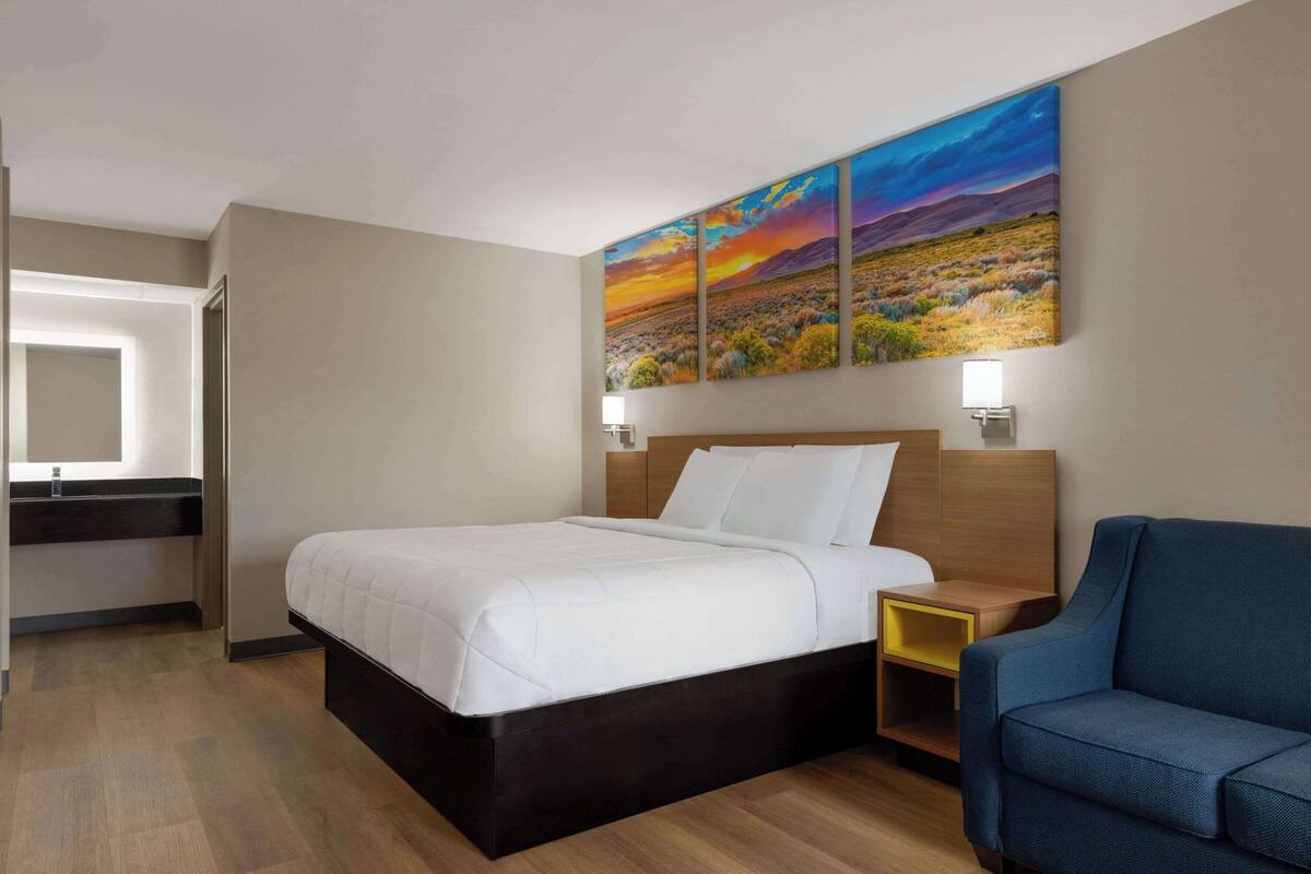 Ein Hotelzimmer mit einem Bett, einem Nachttisch, einem blauen Sessel und einem Wandbild.
