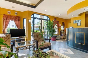 A hotel lobby with a reception desk, seating area, television, and potted plants. - Econo Lodge Inn And Suites (Belleville)