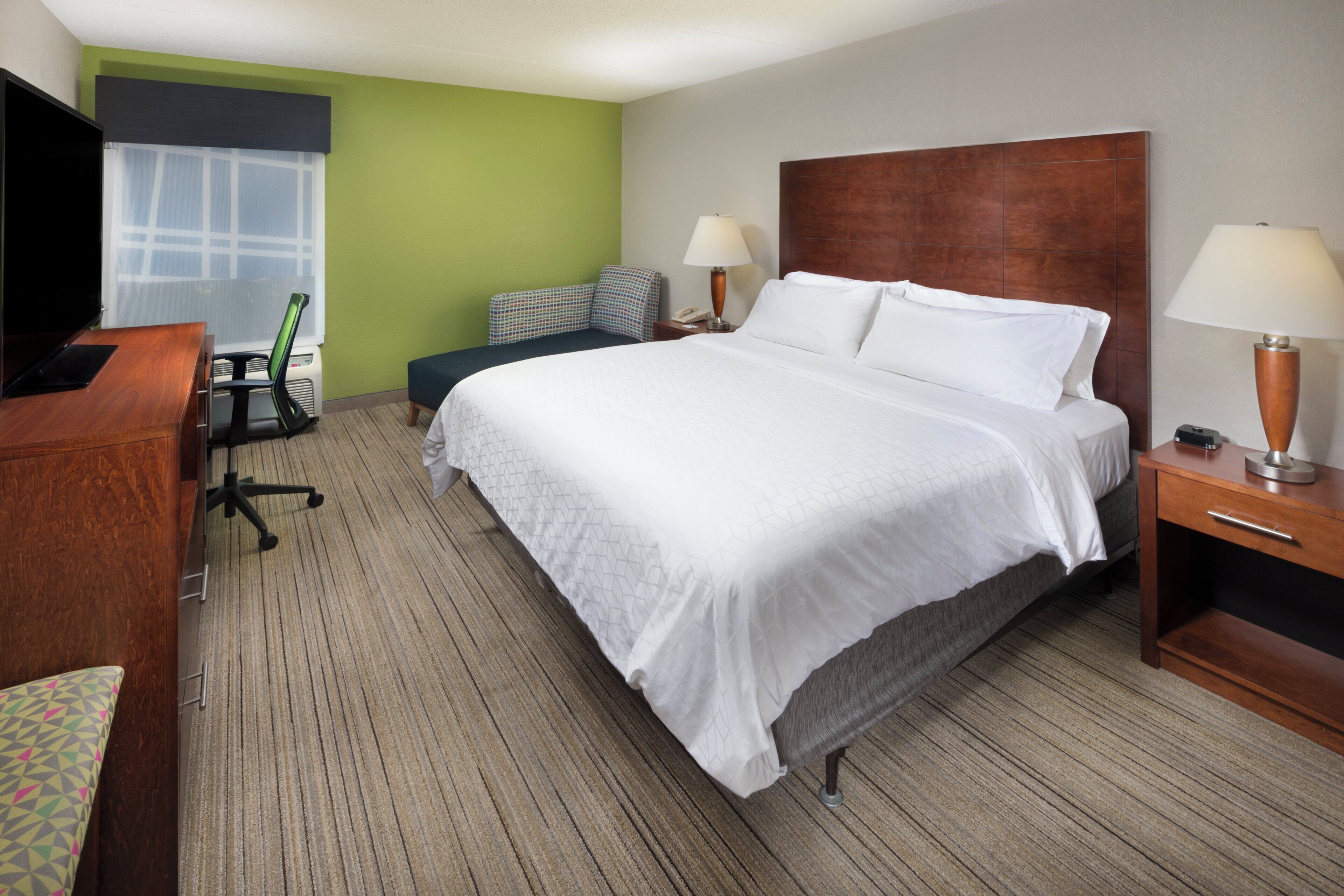 A hotel room with a large bed, a desk, a chair, a lamp, and a television.