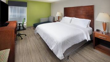 A hotel room with a large bed, a desk, a chair, a lamp, and a television.