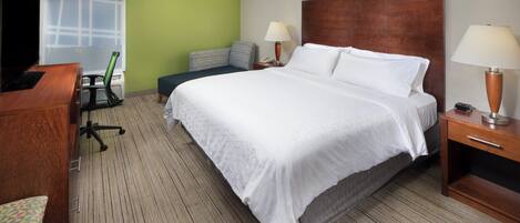 Ein Hotelzimmer mit einem großen Bett, einem Schreibtisch, einem Sessel, einer Lampe und einem Fernseher.