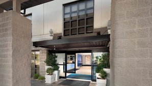 A hotel entrance with a covered walkway, potted plants, and a reception area.
