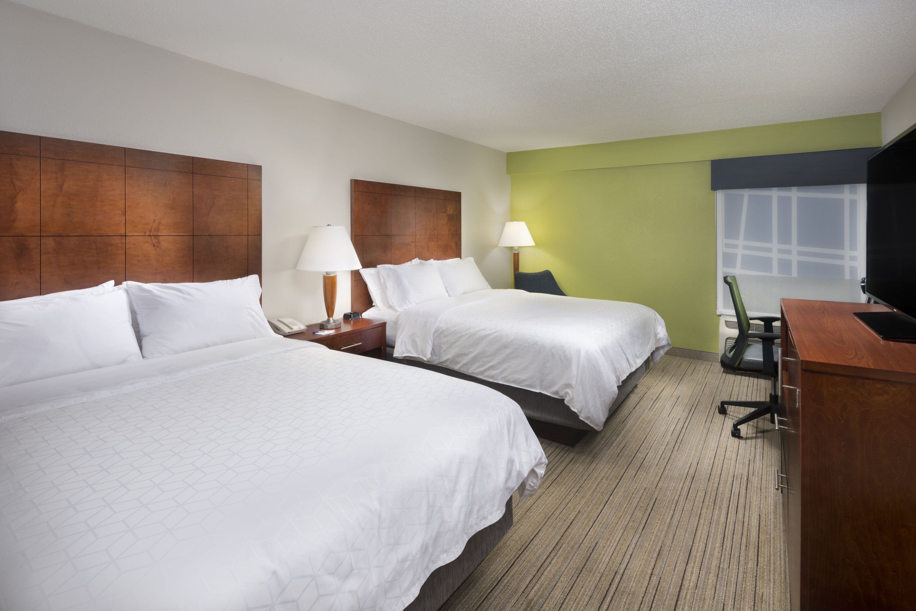 A hotel room with two beds, a desk, a television, and a window.