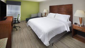A hotel room with a large bed, a desk with a computer, a chair, and a TV.