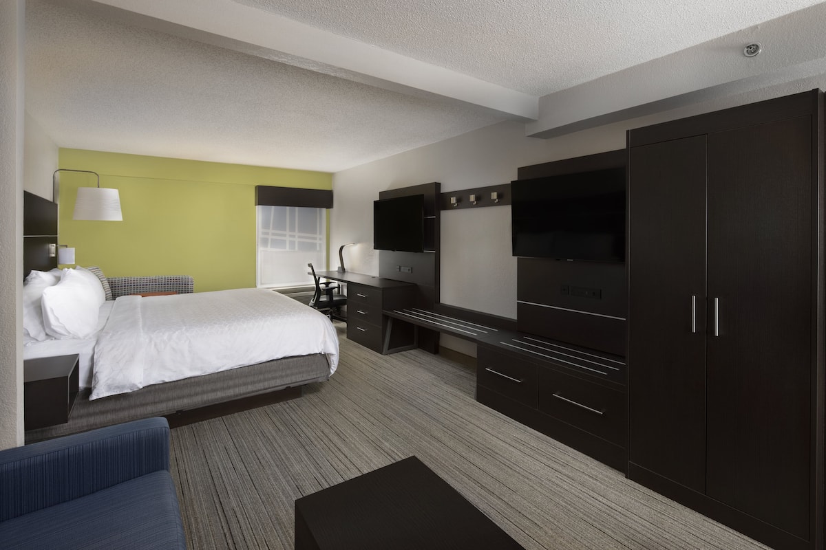 A modern hotel room with a bed, a desk, a TV, and a wardrobe.