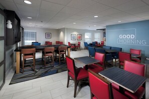 Un espace repas moderne avec plusieurs tables et chaises, un mur d’accent bleu orné du texte « BONJOUR », et un tapis à motifs.