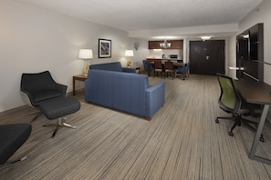 A hotel room with a blue sofa, a dark armchair, a small desk, and a dining table with chairs. - Holiday Inn Express Middlesboro by IHG (Middlesboro)