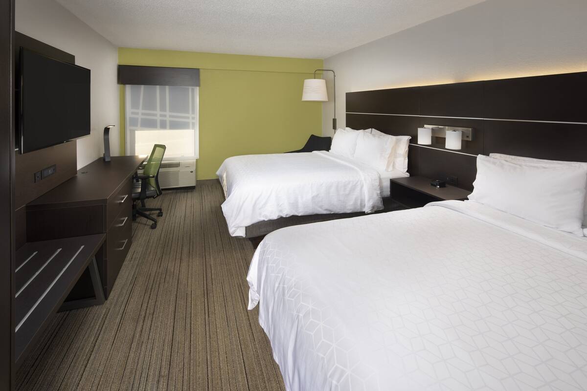 A hotel room with two beds, a desk, a chair, a TV, and a window with blinds.