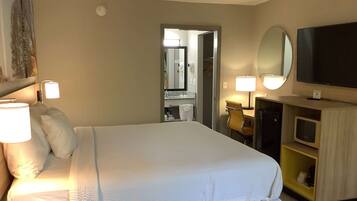 A hotel room with a large bed, bedside lamps, a TV, a mirror, and a bathroom visible through an open door.
