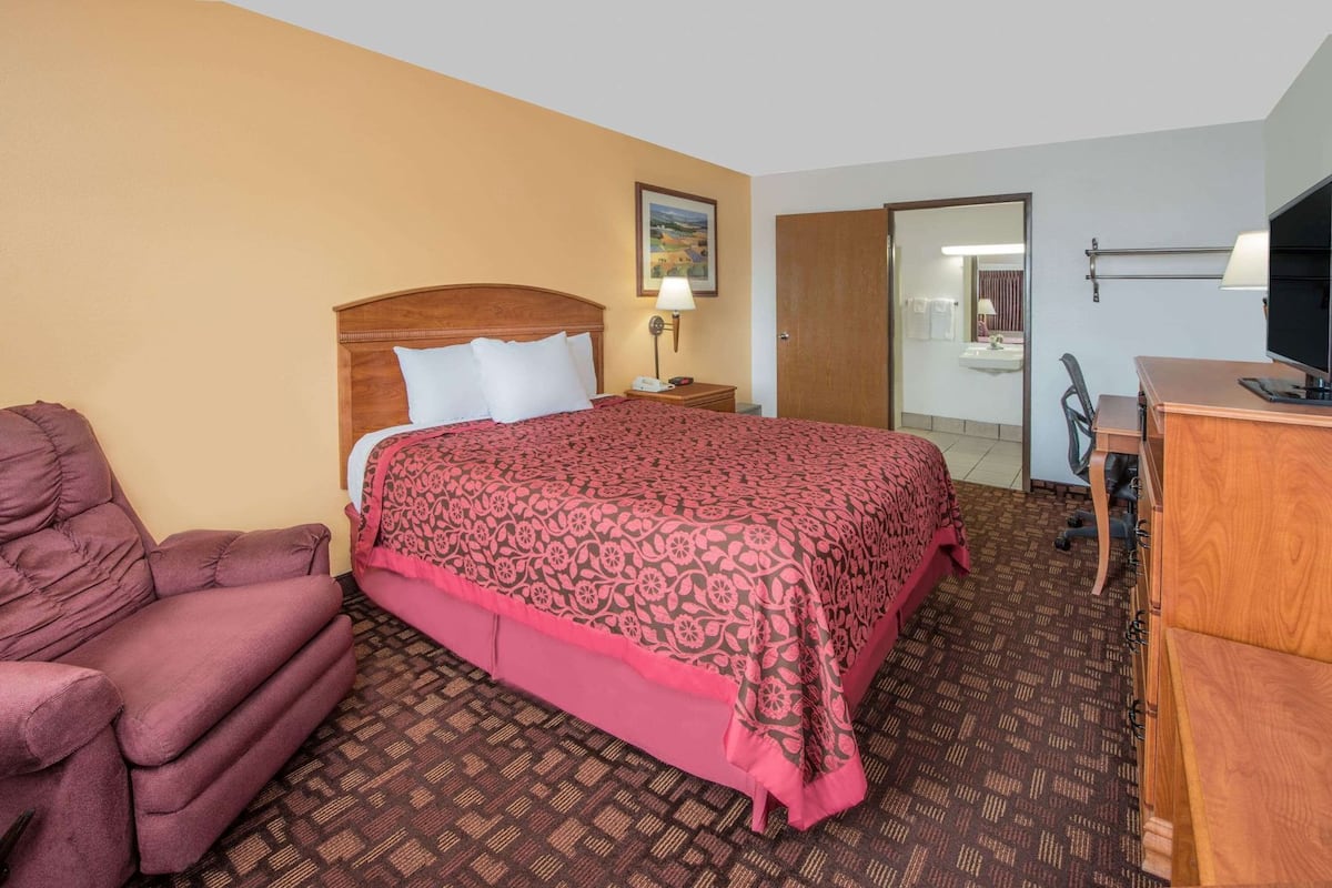 A hotel room with a bed, a desk, a chair, a nightstand, and a painting on the wall.