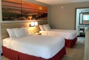 A hotel room with two beds, a painting of a sunset, a bedside table with a lamp, and a bathroom visible through an open door. - Days Inn by Wyndham Kingdom City (Kingdom City)