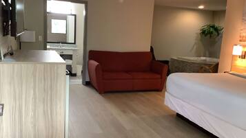Habitación de hotel con piso de madera, un sofá rojo, una cama con ropa blanca, una mesita y un espejo sobre el sofá.