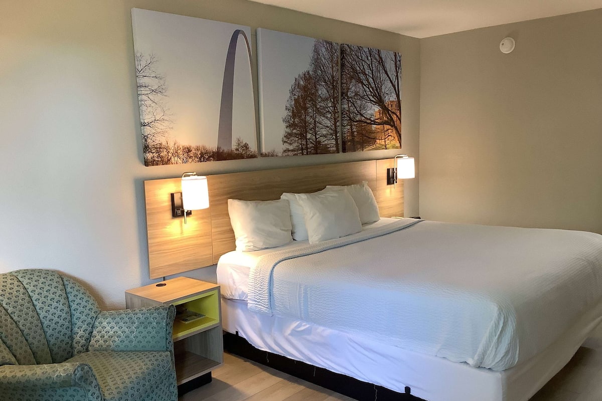A hotel room with a large bed, two bedside tables with lamps, a chair, and artwork on the wall.
