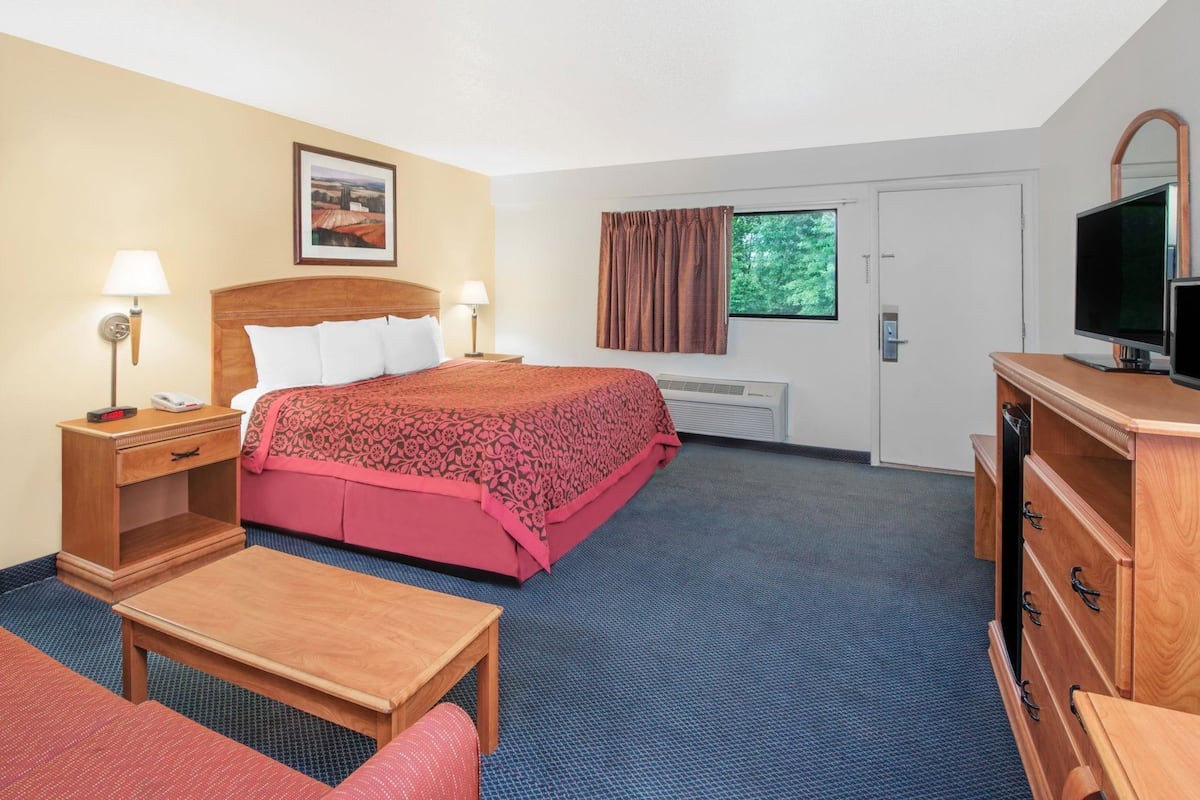 A hotel room with a bed, bedside tables, a desk, a chair, a TV, and a window with curtains.