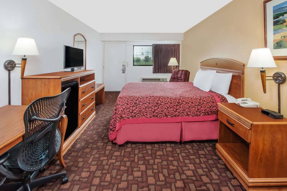 A hotel room with a bed, desk, chair, TV, and a window with curtains.