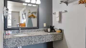 Un baño con lavamanos de encimera de granito, un espejo, toallero y cafetera.