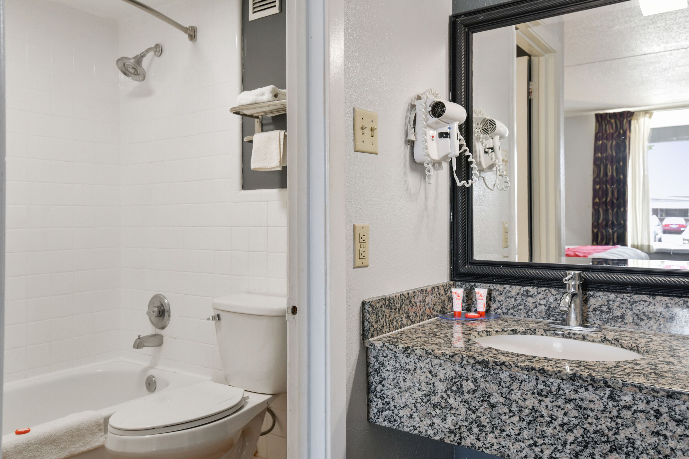 Une salle de bain avec des toilettes blanches, une baignoire, un lavabo en granit, un sèche-cheveux et un miroir.