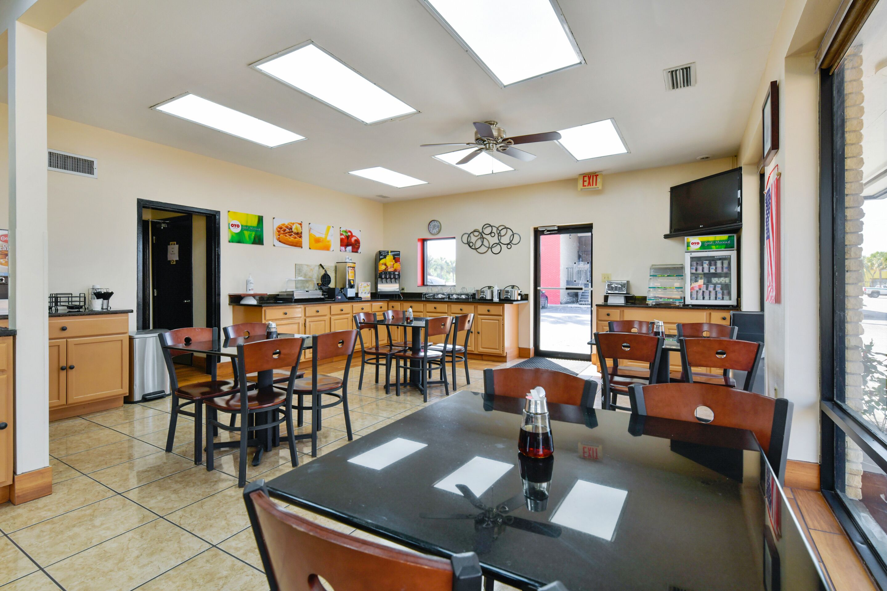 A restaurant with a large dining area, multiple tables and chairs, a ceiling fan, and a window with a view of the outside.