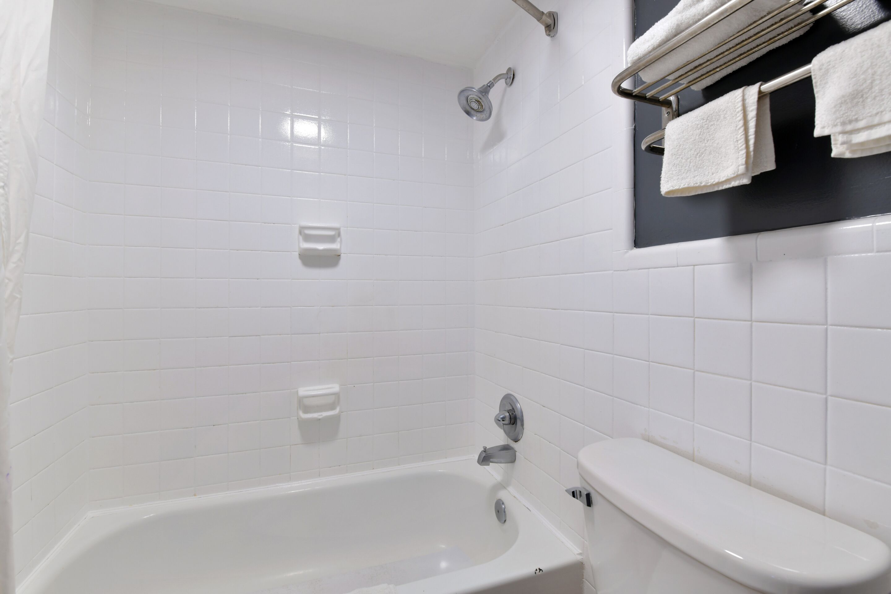 A bathroom with a white bathtub, a toilet, and a towel rack with towels.