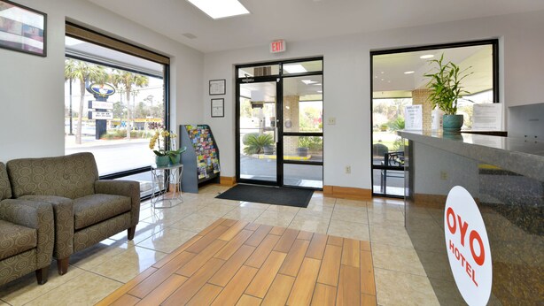 A hotel reception area with a reception desk, a couch, a potted plant, and a view of the outside. - OYO Hotel Lake Park/Valdosta I-75, Exit 5 (Lake Park)
