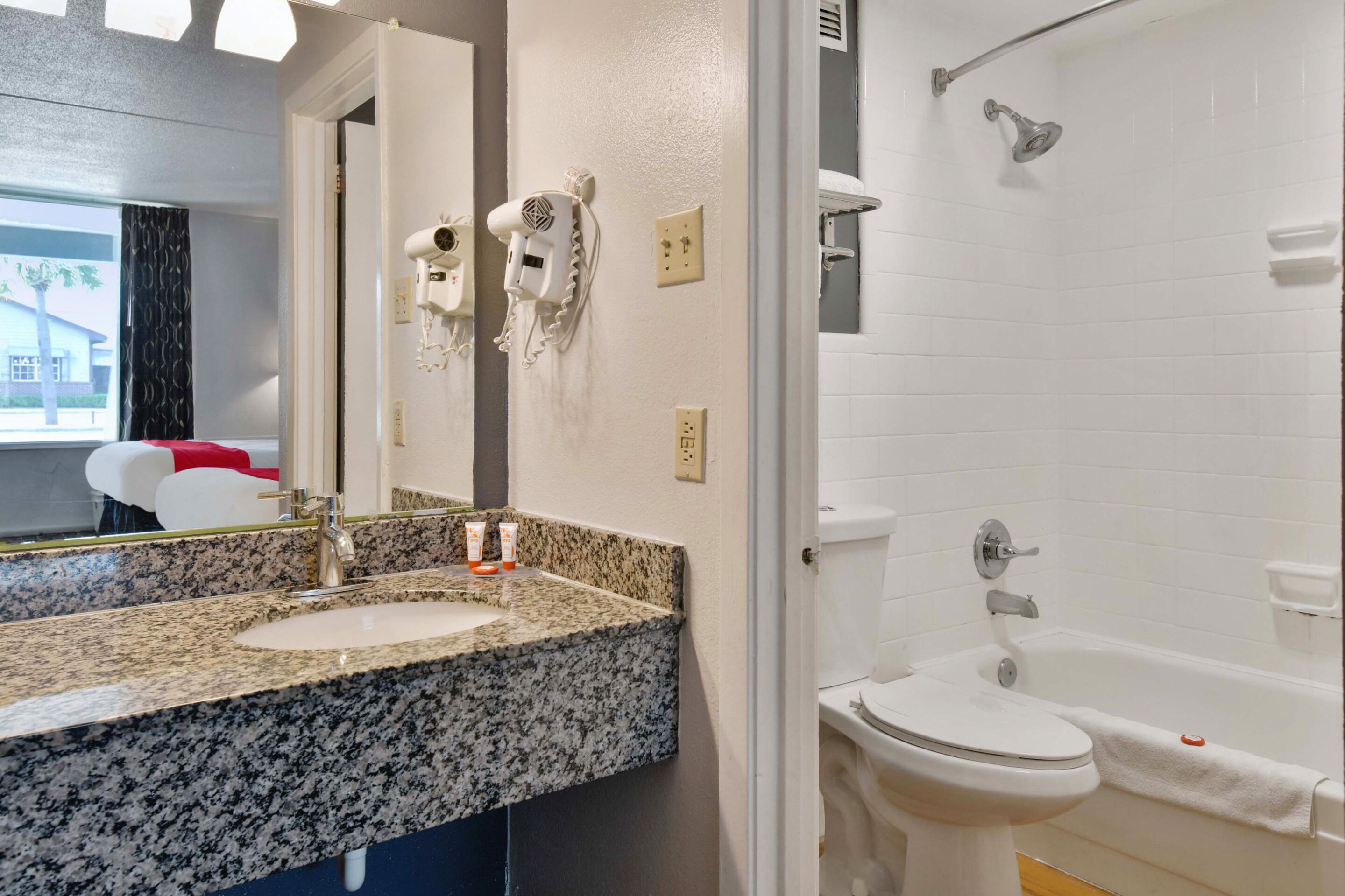 A bathroom with a granite countertop sink, a white toilet, and a shower.
